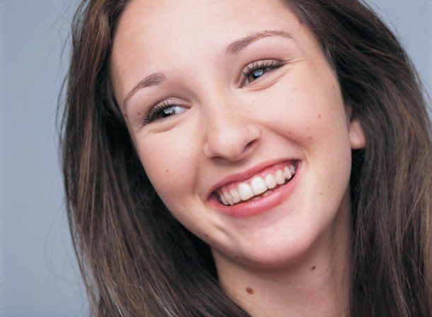 Smiling woman with dark hair in professional headshot against neutral gray background for dental practice.