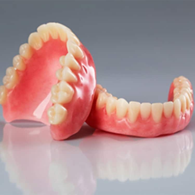 Complete dentures displayed showing upper and lower dental prosthetics against gray background.